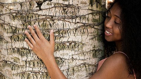 Lächelnde Frau umarmt einen Baum